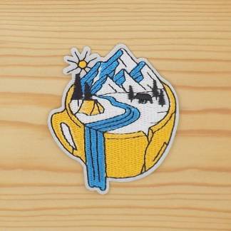 Iron-on embroidered patch featuring a camping scene inside a yellow mug